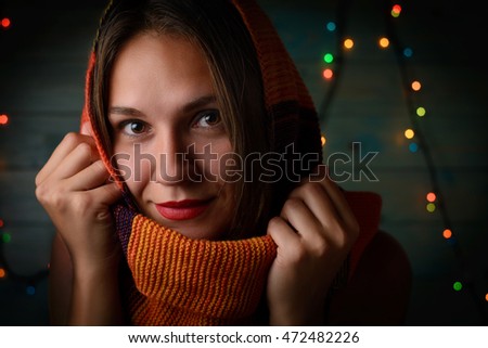 Portrait of beautiful young smiling girl in a red scarf on the background of the winter night christmas lights