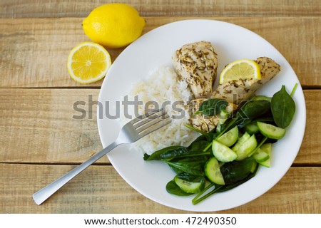 Green spinach and cucumber salad, white rice and chicken fillet baked with thyme and lemon and served on a white plate. Top view