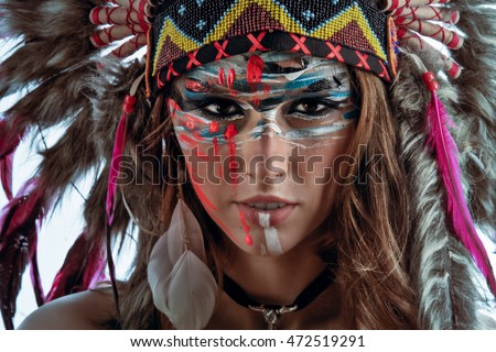 A model wearing Native American hat feather roach. Beautiful face with wild creative colorful makeup.  Indigenous peoples of the Americas outfit. Closeup portrait. Ethnic woman with feathers on head