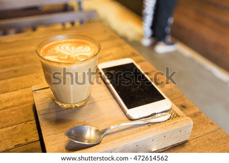 Cup of lattecoffee on a wooden table with smartphone in art cafe