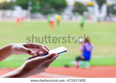 Man use mobile phone, blur image of  woman photographed footballer as background.