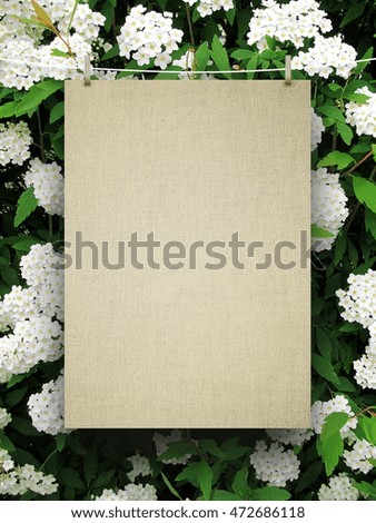 Close-up of one blank brown canvas frame hanged by pegs against white flowers and green leaves background