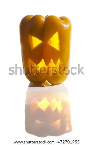 Food art creative concept. Halloween scary face carved into a yellow capsicum vegetable with back light over a white background.