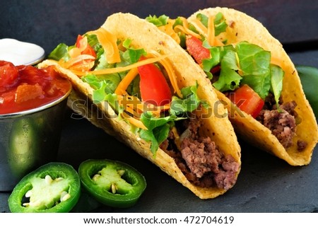 Hard shelled tacos with ground beef, lettuce, tomatoes and cheese close up, on slate background 