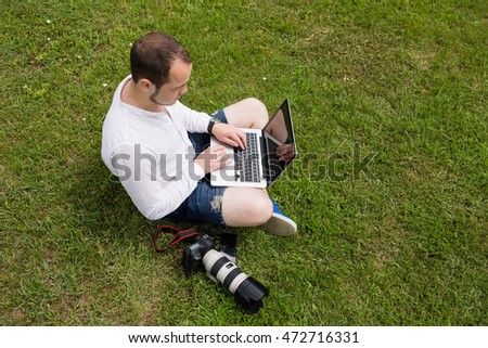 A photographer working on a laptop outdoors on green grass