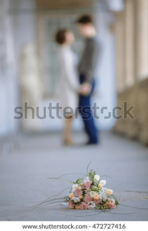 Wedding bouquet lies on the grey ground while young couple stands on the background