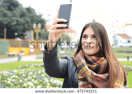 Portrait of a young beautiful woman taking selfie with her smartphone. Outdoors.
