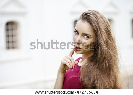 Young beautiful brunette woman has put forefinger to lips as sign of silence, outdoors