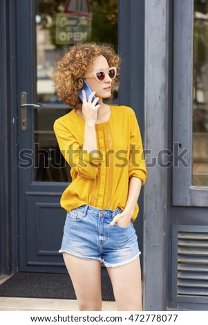 Portrait of young casual businesswoman making call while standing in front of her small coffee shop.