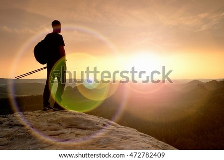 Thinking hiker in black on rocky peak. Wonderful daybreak. Ginger hair man in black at the end of sharp cliff above deep valley. Strong lens defect, reflection