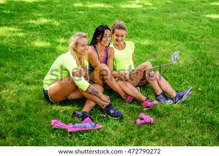 Three attractive sporty females sitting on a lawn and doing selfie after fitness workouts.