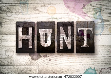 The word "HUNT" written in vintage dirty metal letterpress type on a whitewashed wooden background with ink and paint stains.