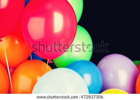 Group of glossy colorful balloons over black wall background, vintage tonal correction filter, retro stylized photo