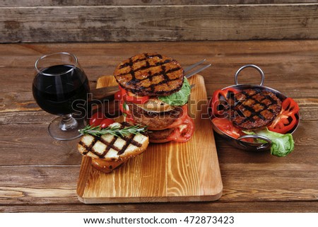 fresh grilled beef double huge hamburger served on wooden plate with wine cherry tomatoes and rosemary over table