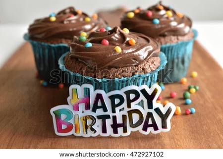 Chocolate birthday cupcake with chocolate frosting and sprinkles on wooden.