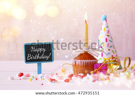 Birthday concept with cupcake and candle next to little chalkboard on wooden table. Glitter overlay. Selective focus