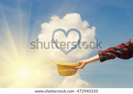 The hand of a young girl holding a straw hat against the blue sky. Heart sign