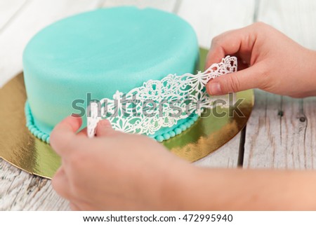 Preparing elegant wedding cake with turquoise mastic and white lace icing