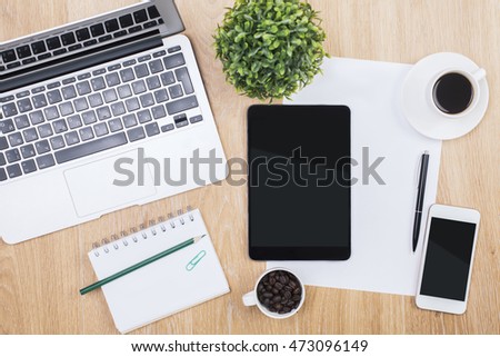 Top view of wooden office desktop with tablet, smartphone, laptop, decorative plant coffee beans and drink, spiral notepad and other items. Mock up
