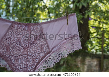 Pink lace woman's shorts dry on the rope in the summer in the day with green leaves as background