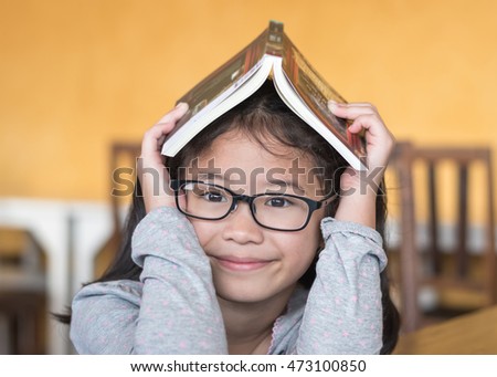 Educational literacy, world book day concept with smart Asian school student kid with eyeglasses having children book over her head Royalty-Free Stock Photo #473100850