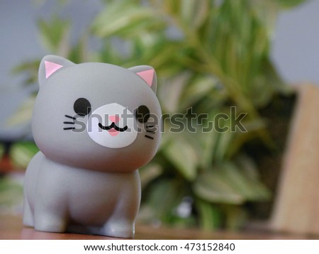Cute gray cat made from plastic with blurred plant background. Close up angle facing left  - Landscape.