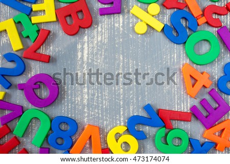 Border of colorful toy magnetic letters and numbers over a  grey wooden background