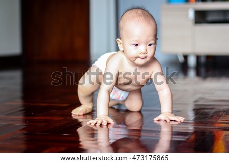 Cute adorable little Asian 8 months old baby boy child wearing diaper try to crawling on wood floor in living room at home, photo in real life interior, Soft and Selective focus