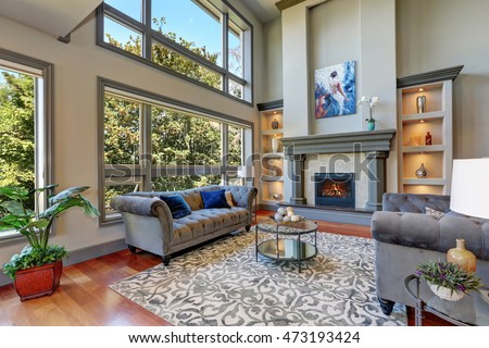 Grey interior of high vaulted ceiling family room in luxury house with fireplace and large windows. Northwest, USA. Royalty-Free Stock Photo #473193424