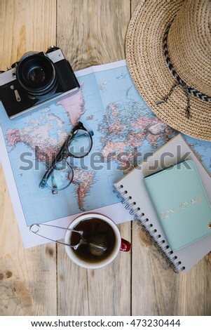 Travel preparations essentials. World map, cup of tea, vintage film camera, hat, passport, notebook and stylish glasses on the old rustic wooden table background, flat lay