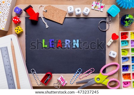 Small blackboard surrounded with various stationary with the word Learn in the middle, on wood background