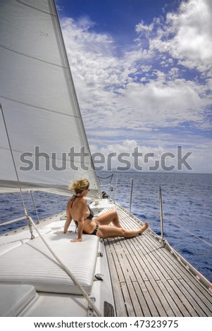 Attractive woman sitting on the front of large and luxurious sailboat sailing through the tropics.