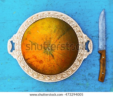 ripe melon on a golden platter and knife on old blue table, top view close-up