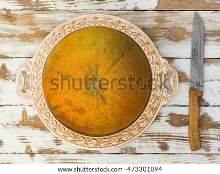 ripe melon on a golden platter and a knife on an old white table, top view close-up