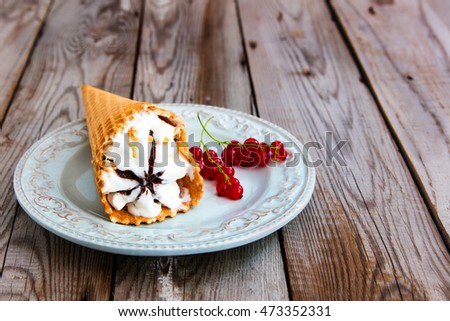Ice cream with red currant in a waffle cone on wooden background.