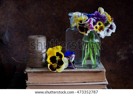 Pansies in glass bottles, a ball of twine and old books on a wooden background