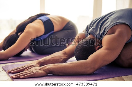 Beautiful Afro American couple in sports clothes is stretching on yoga mat while working out at home Royalty-Free Stock Photo #473389471