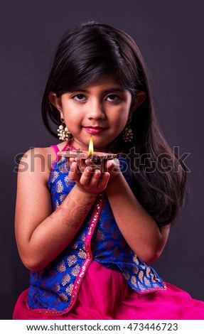 Cute little indian/asian girl in traditional wear holding a diya or Terracotta oil lamp on Diwali festival. Front view over black background Royalty-Free Stock Photo #473446723
