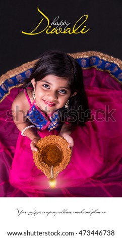 Diwali Greeting Card showing Cute little indian/asian girl in traditional wear holding a diya or Terracotta oil lamp. top view over black background Royalty-Free Stock Photo #473446738