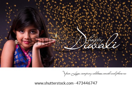 Greeting card showing Cute little indian/asian girl in traditional wear holding a diya or Terracotta oil lamp on Diwali festival. Front view over black background Royalty-Free Stock Photo #473446747