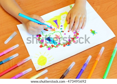 Child draws felt-tip pens. Small child holds a blue felt-tip pen in hand and draws abstract princesses castle. A kids drawing, a set of colored felt pens on a wooden table. Kindergarten art background