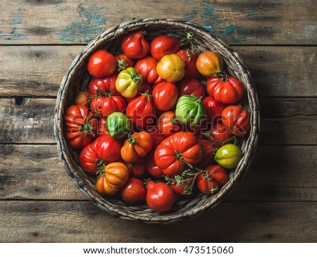Fresh colorful ripe Fall heirloom tomatoes in basket over wooden background, top view, horizontal composition Royalty-Free Stock Photo #473515060