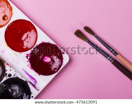 A set of paints and brushes for art on a pink background