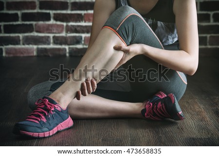 have a leg cramp in fitness exercise training, healthy lifestyle concept, indoors gym wooden floor brick wall background Royalty-Free Stock Photo #473658835