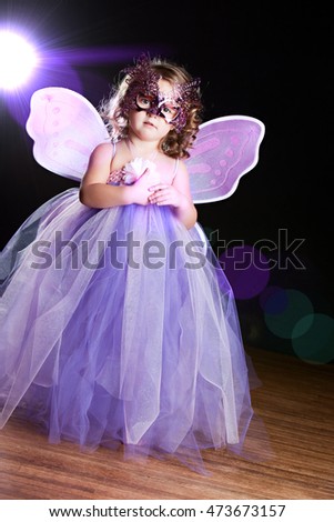 Magical! Adorable toddler wearing a long tutu dress, butterfly wings and mask. Background light and lens flare for dramatic effect. 