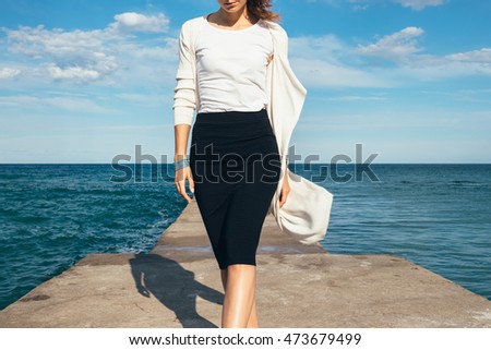 Elegant woman in a skirt and cardigan walks on the background of the sea on a sunny day