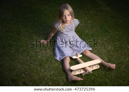 Child blond girl dreams of traveling and playing with an airplane in outdoor in the summer