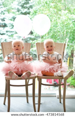 Two baby girl identical twin sisters. decorated birthday cake wearing pink crown and bunting tasty flowers in the background about to break and smash cake