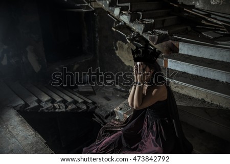 photo of a jester woman holding hands near face while sit inside a dark stone staircase deep inside the basement of a vintage haunted castle. Halloween concept