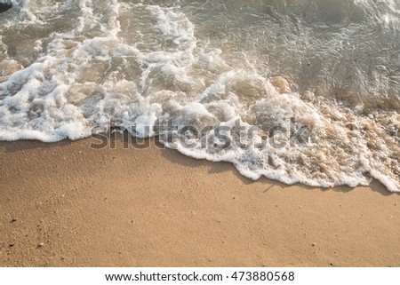 Soft wave of the sea on the sand beach with sunlight. Tropical sandy beach background with copy space. Top down view.